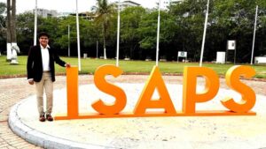 Dr. Ashish Davalbhakta standing beside large ISAPS letters at an international event